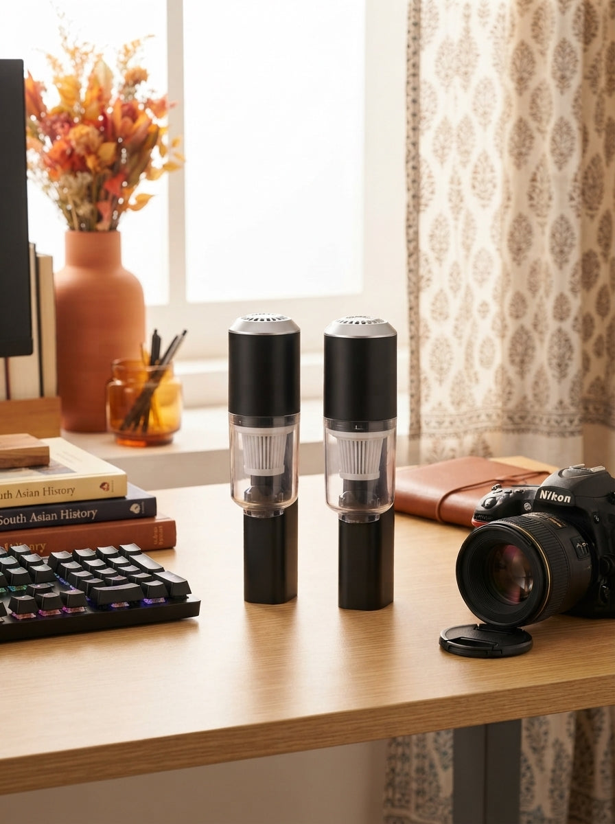 Two multifunctional air dusters resting on a desk beside a mechanical keyboard and camera lens in a bright, modern workspace.